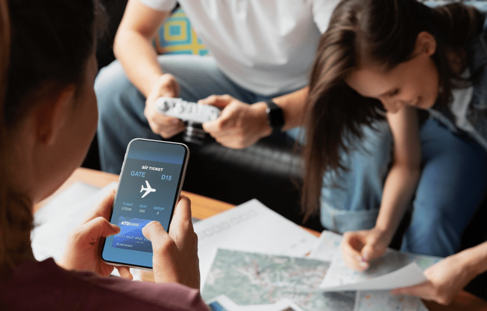 Travelers checking a digital boarding pass on a phone while planning a trip together with maps and notes on a living room table.